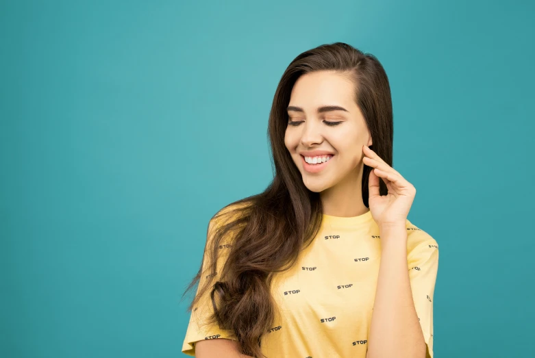 a girl in a yellow shirt smiles as she looks at her hand near her ear