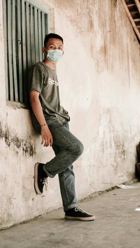 a man with a face mask leaning on the side of a building