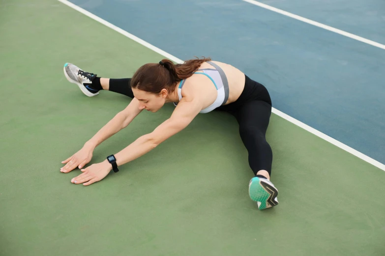 a woman stretches her legs on a tennis court