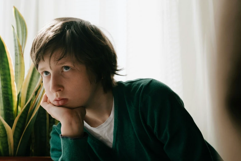 the boy is sitting in front of the plant and looking at soing