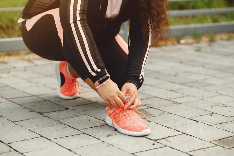 a woman tying her running shoelaces while sitting on a brick walkway