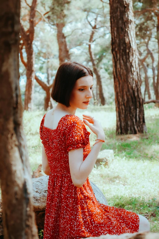 a woman in a red floral dress sitting in the woods