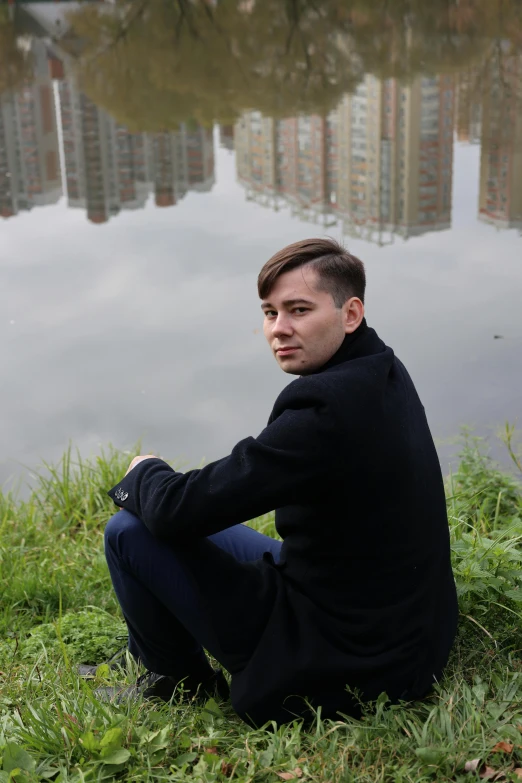 a man sitting next to the water on top of a green field