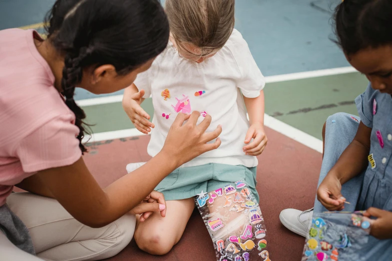 three girls sitting on the floor, one is touching a child's finger