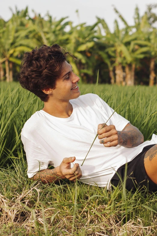 a man that is sitting in the grass with a flower