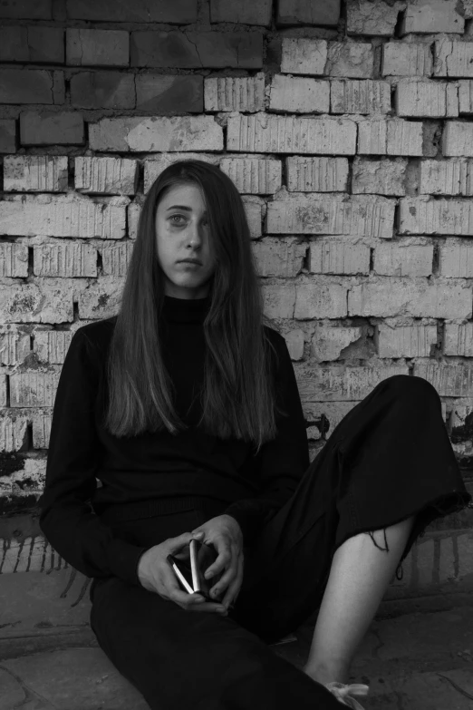 a woman sitting on the floor in front of a brick wall