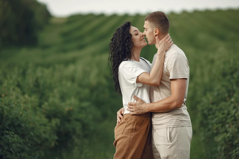 a man and woman kissing while they walk through a lush green field