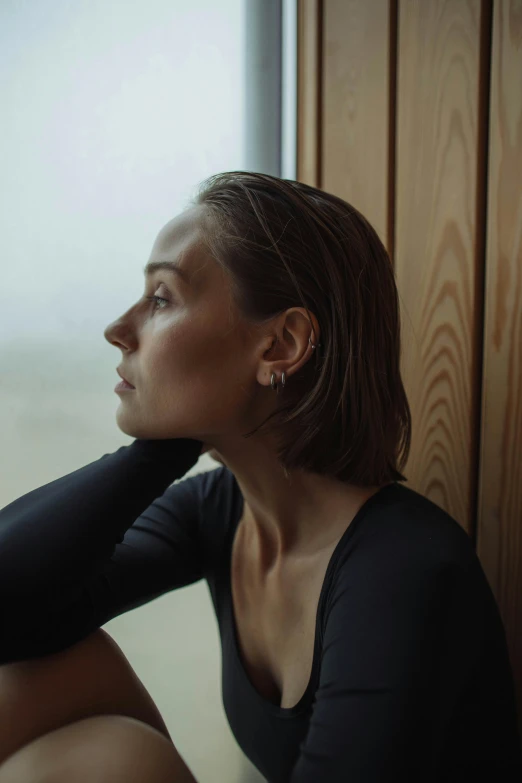 a young woman wearing a black shirt is sitting in front of a window