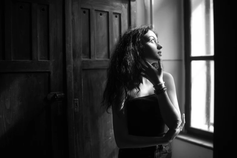 a young woman stands in a dark room, holding her hand against her face