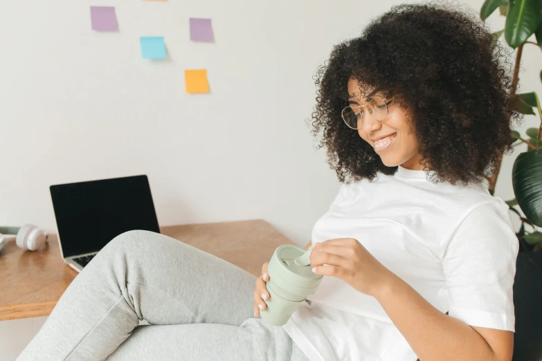 a woman in white is sitting on a chair drinking from a mug