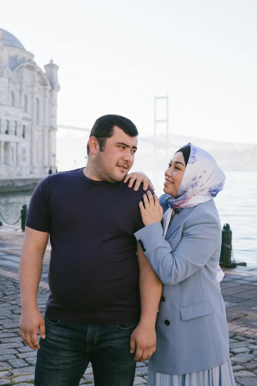 a couple is standing by the water smiling for a po