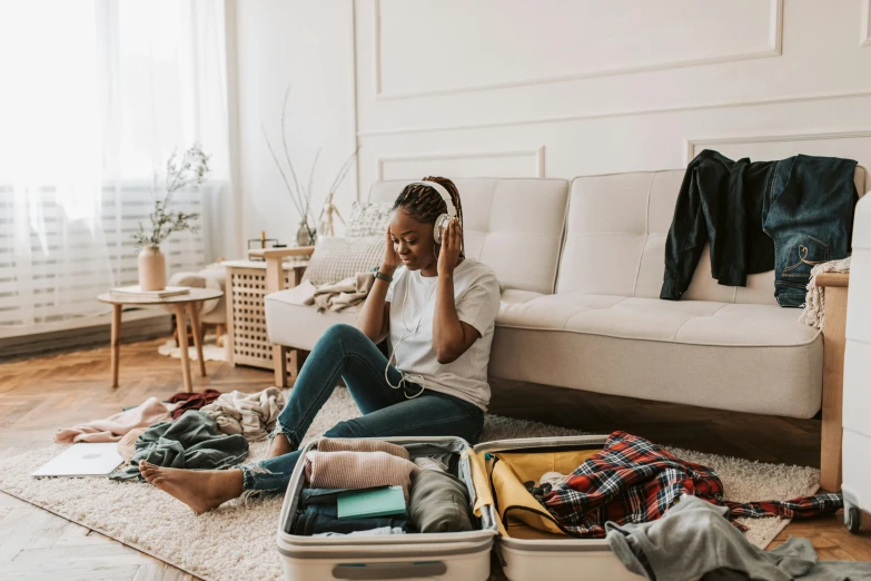 a woman is sitting on the floor in front of a suitcase filled with clothing