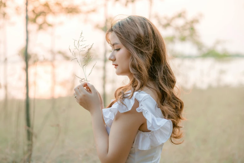 a woman is standing in a field and smelling a flower