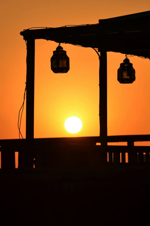 three lanterns hang over a deck during sunset