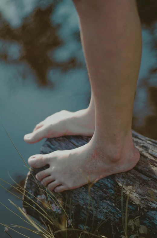 a pair of feet are standing on top of a log by the water