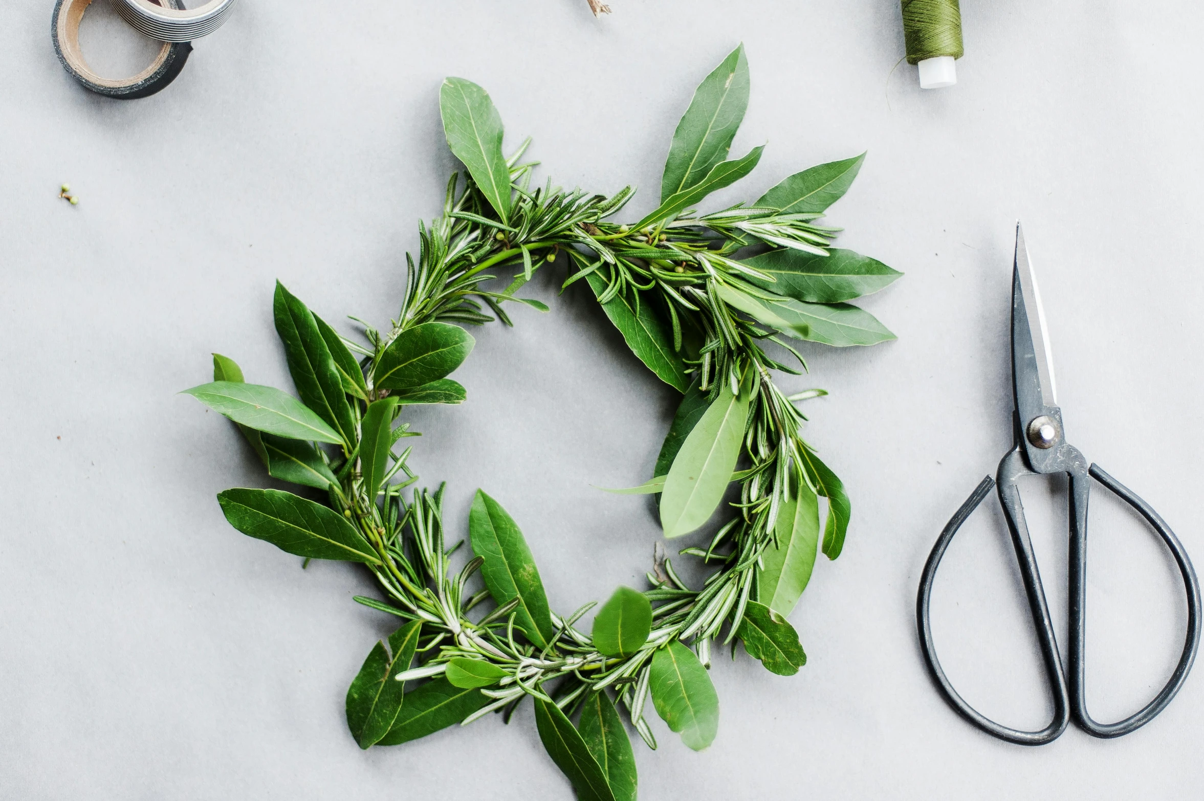 a green wreath with greenery sitting on a table next to scissors