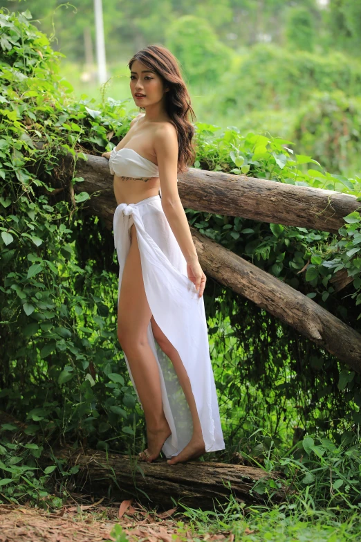 a woman in a white dress standing next to greenery