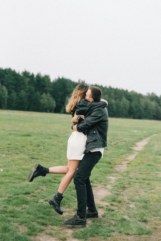 a woman wearing a white dress hugging a man in a field