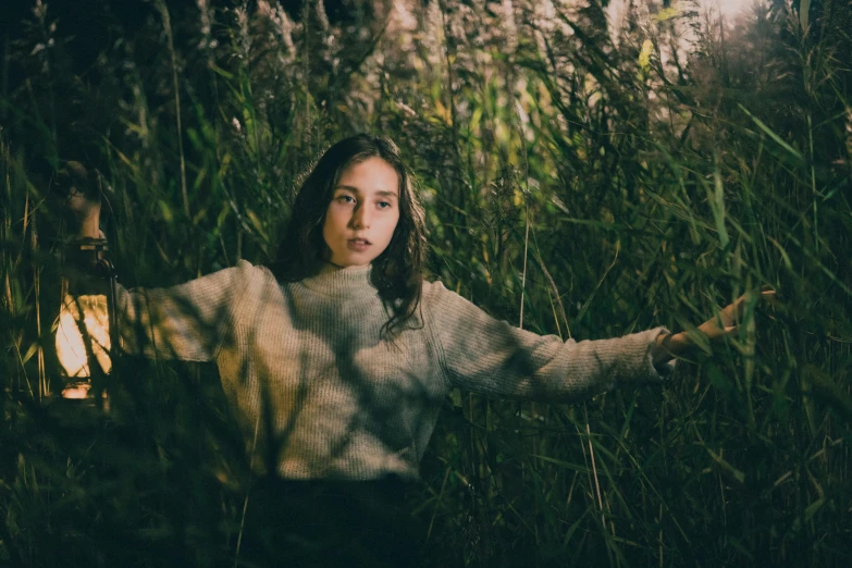 woman in white sweater standing by lantern surrounded by tall grass