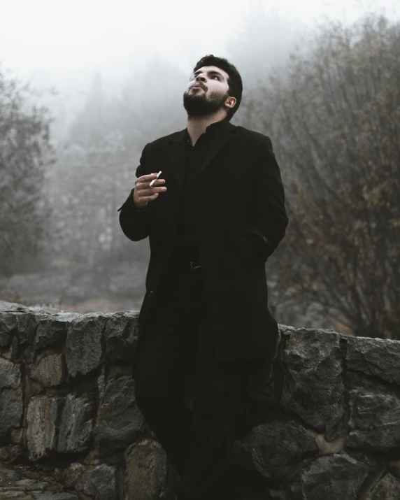 a man in black standing with his hand on the stone wall