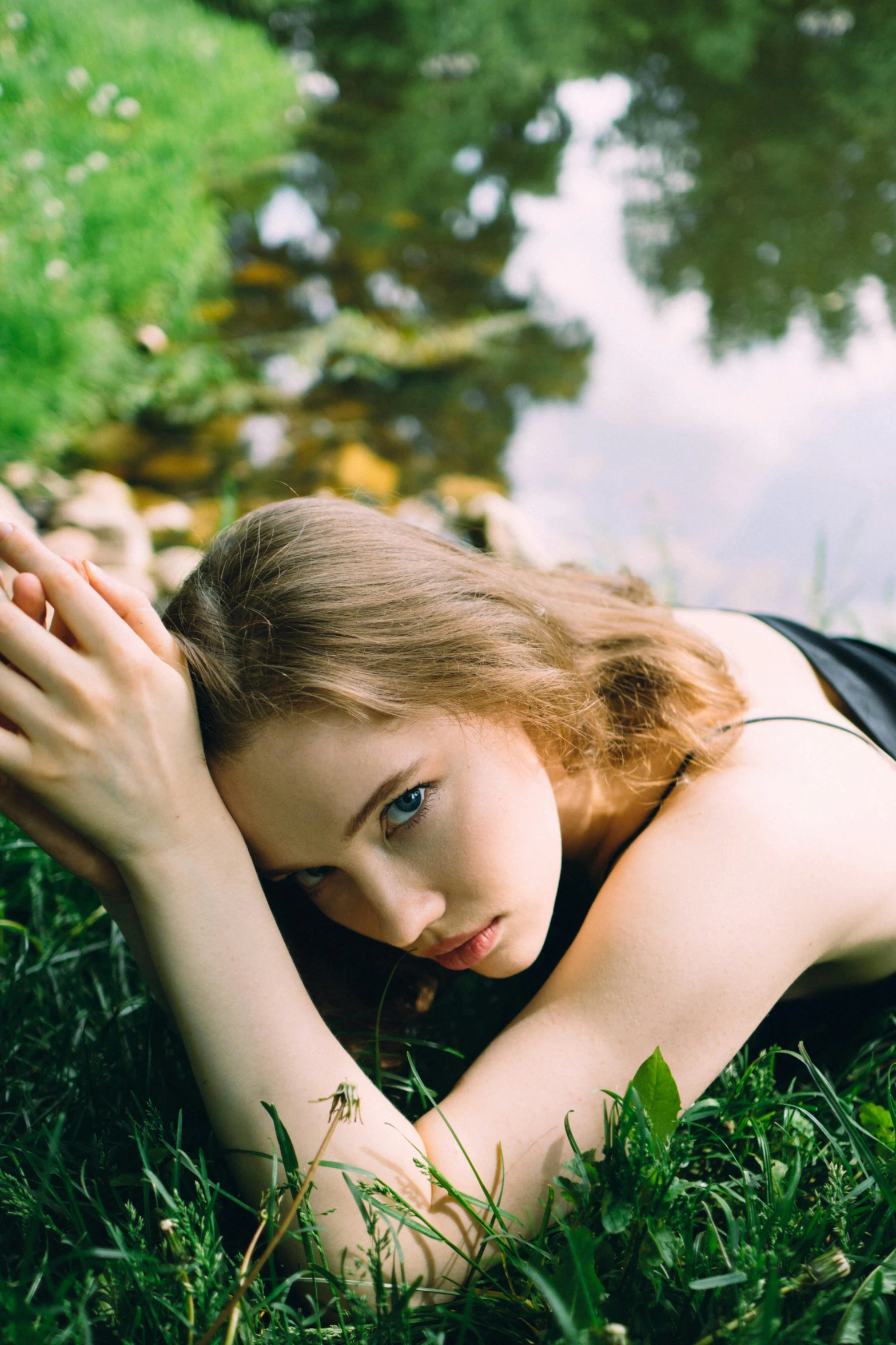 young woman laying on grass by a pond