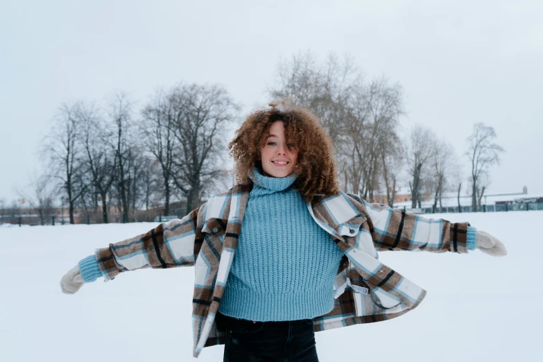 a woman wearing a plaid coat and blue sweater poses for a po in the snow