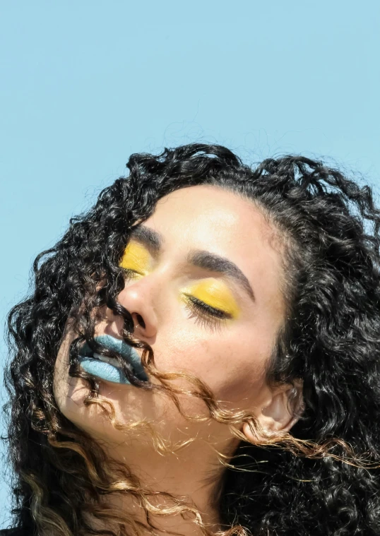 a woman with bright eye makeup holding a tooth brush to her mouth