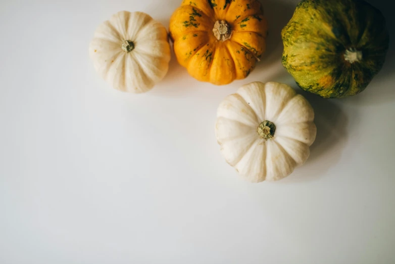 three pumpkins, one yellow and one white, on a counter