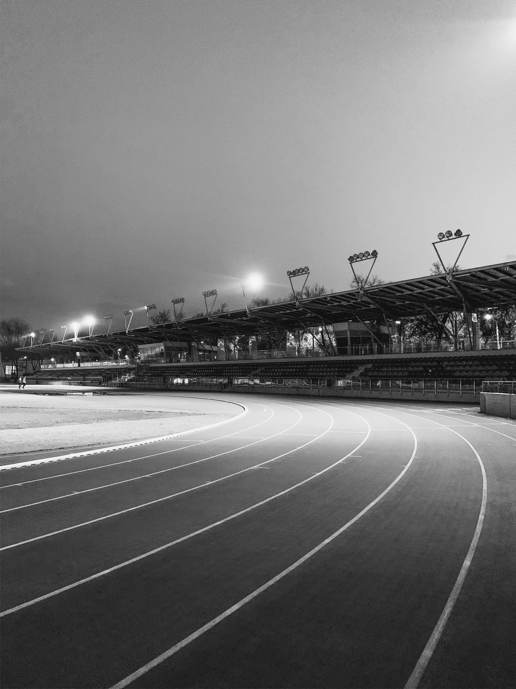 an empty stadium at night with lights on and one man in the distance