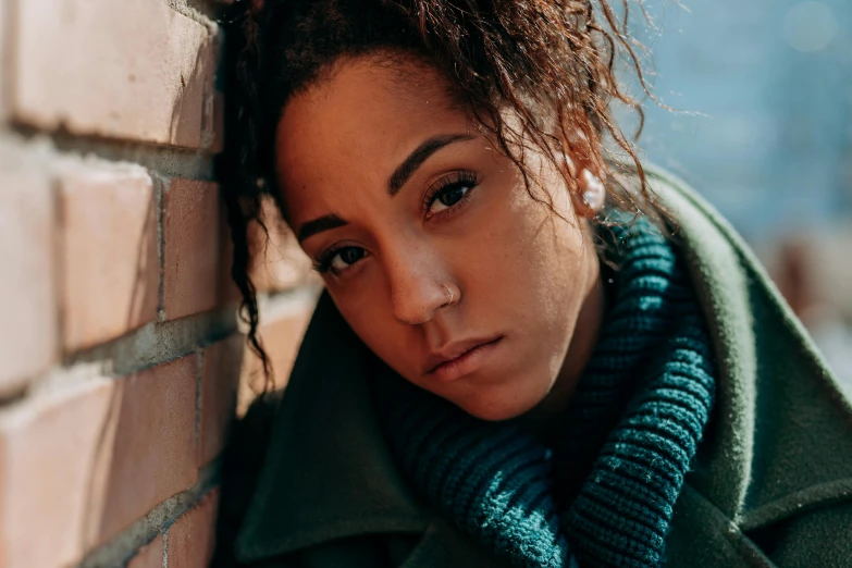 a girl in a green coat leaning against a brick wall