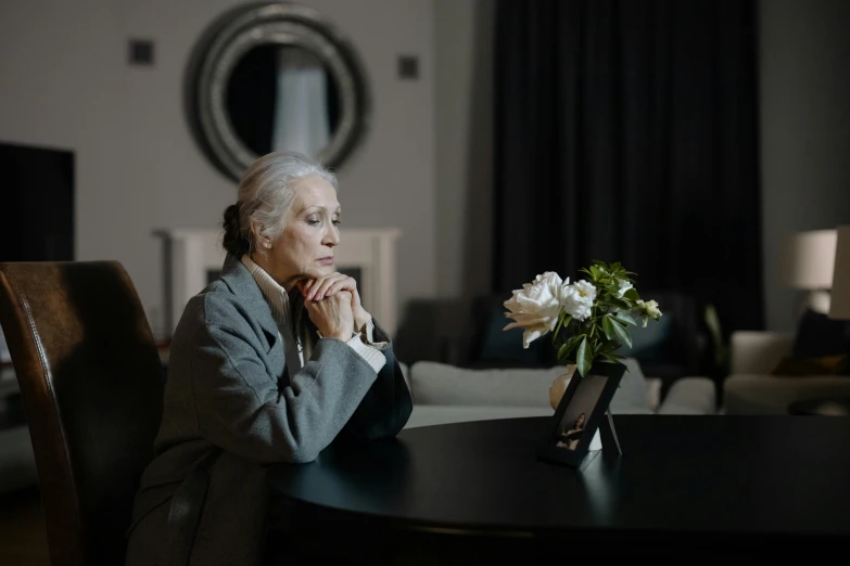 an old woman sitting in front of a small table with flowers