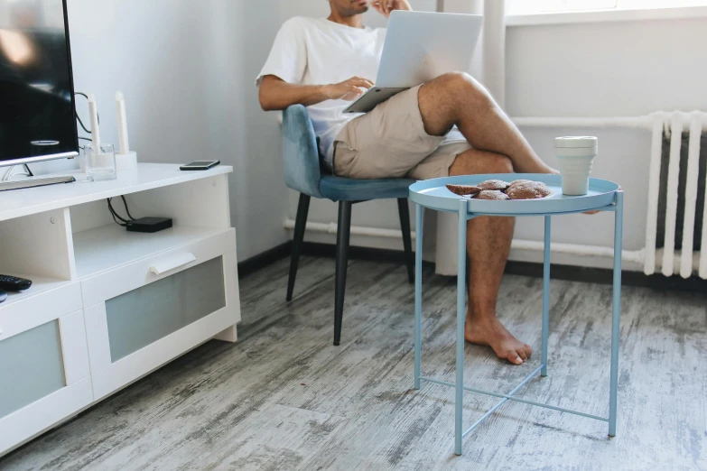 a man in shorts sitting at a blue table with a laptop and a cup