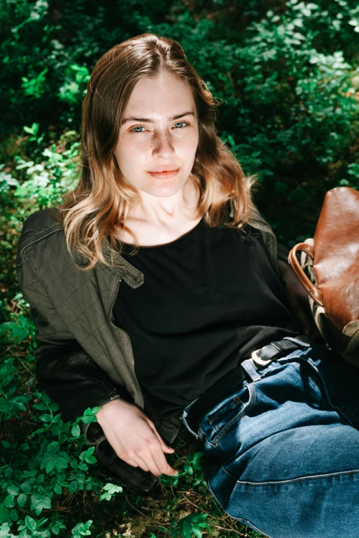 a girl sitting in the grass in front of her purse