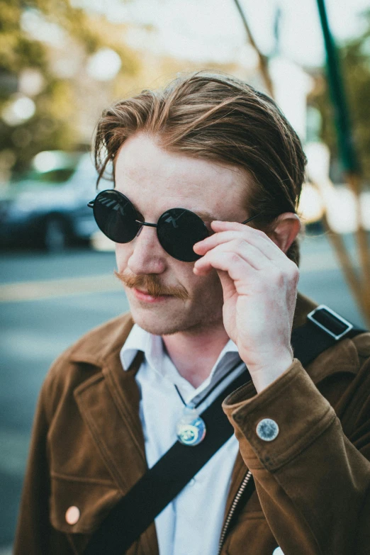 a man wearing dark sunglasses standing on the side of a road