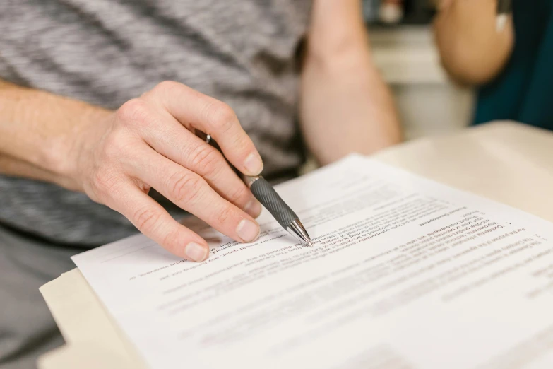 a man holding a black pen while writing on some paper