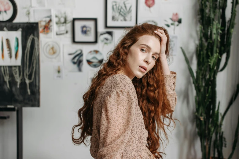 a red headed woman poses in front of a large wall of pictures