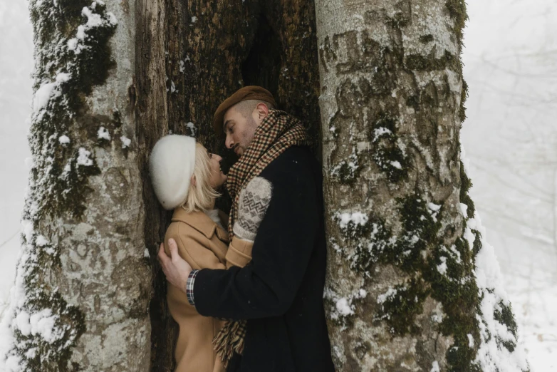 a couple standing in a snow covered forest hugging each other