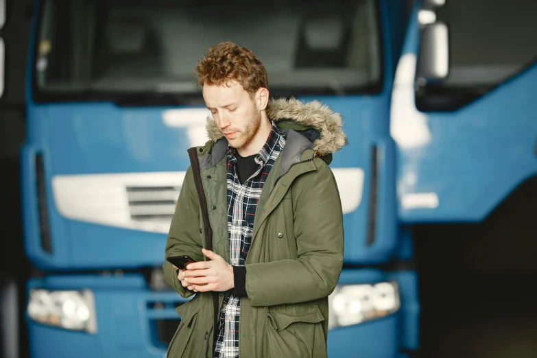 a man looks at his phone in front of a large truck