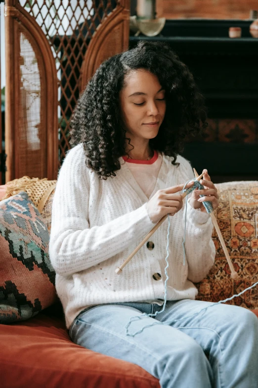 a woman is on the couch knitting and looking at her phone