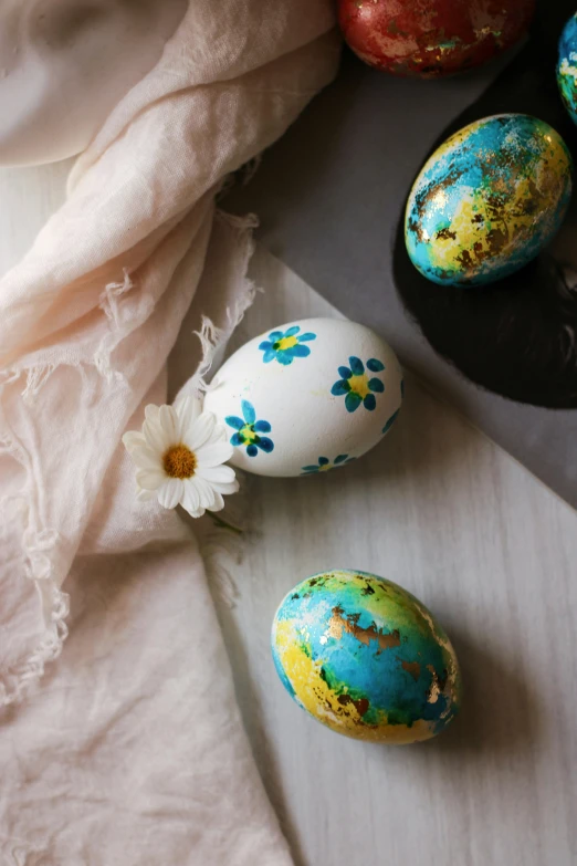 painted eggs on a white cloth next to an orange apple