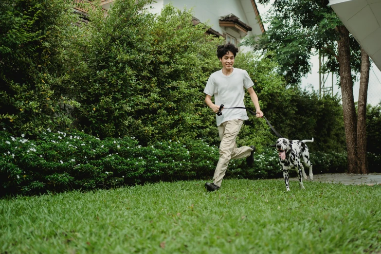 man walking a dog through a yard near some trees