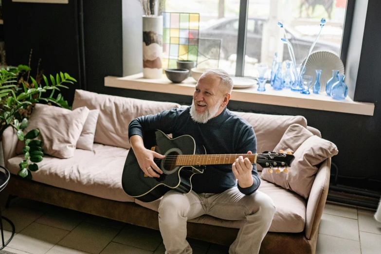 an older man sitting on a couch playing a guitar