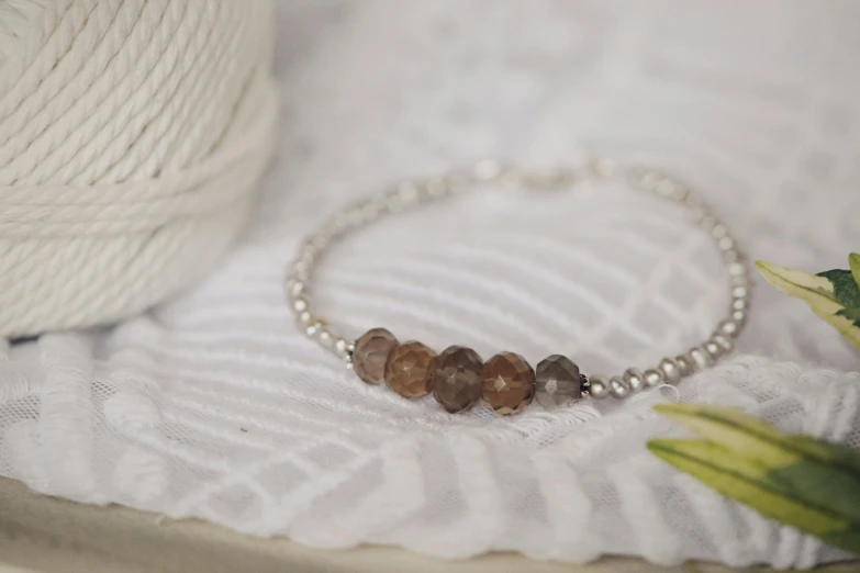 a white yarn ball sits on top of a knit swatched blanket, next to a handmade celet with beads and stones