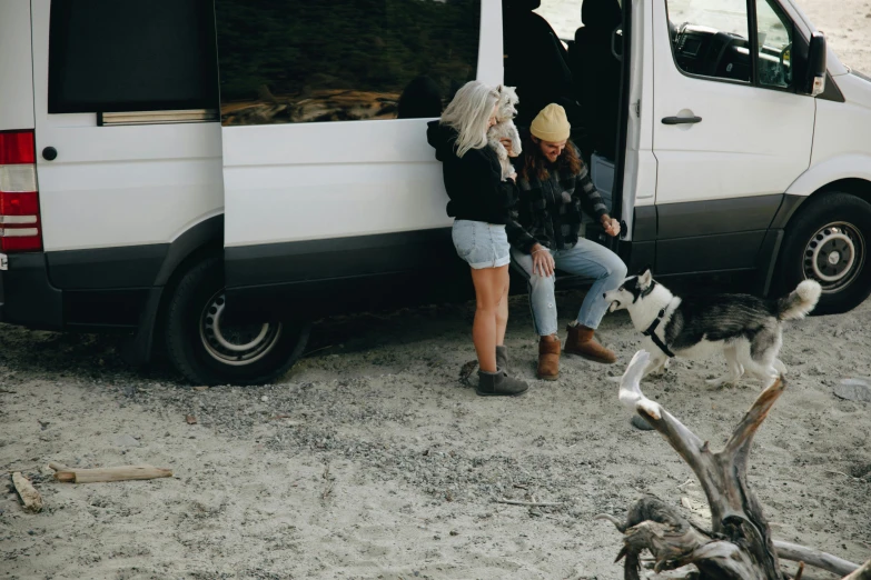 two women and a dog that are sitting in front of a van