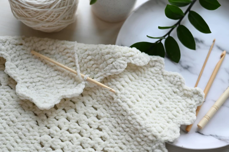 knitted dishcloth and knitting needles next to white ceramic