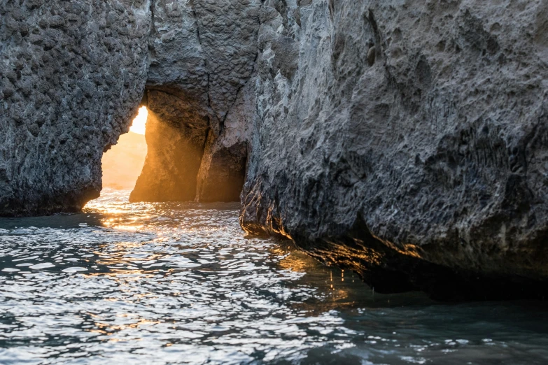 a sun is peeking through the rocks that are along the ocean