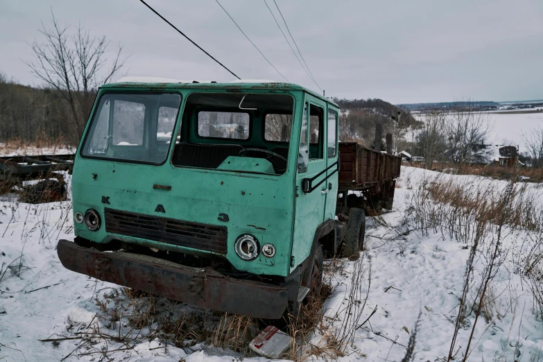 the truck is old and worn, sitting out in a snowy field