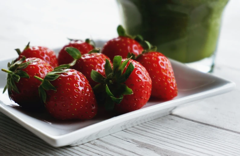 fresh strawberries sit on a white square plate