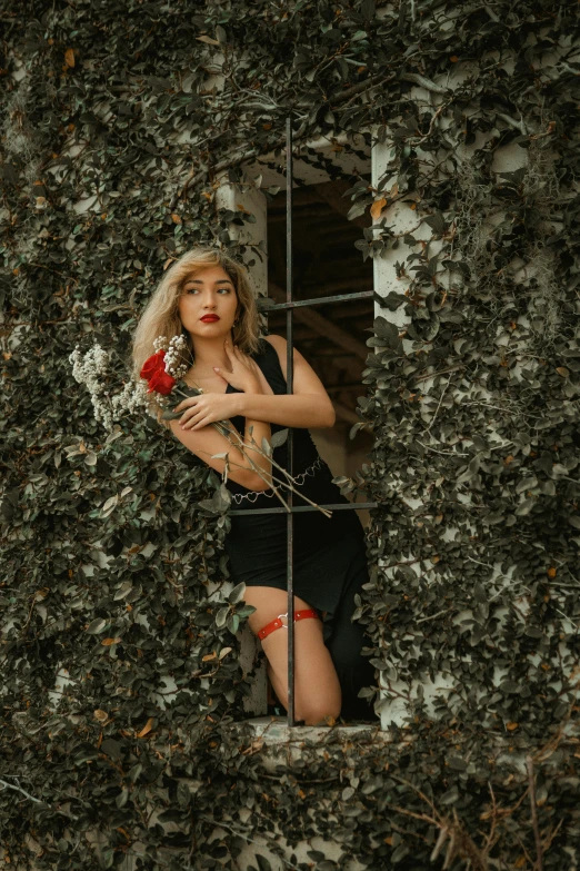 an attractive woman stands in front of a large ivy fence