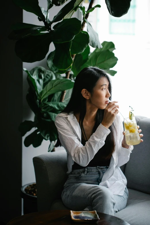 a woman sitting on a couch holding a bottle and talking on a cellphone